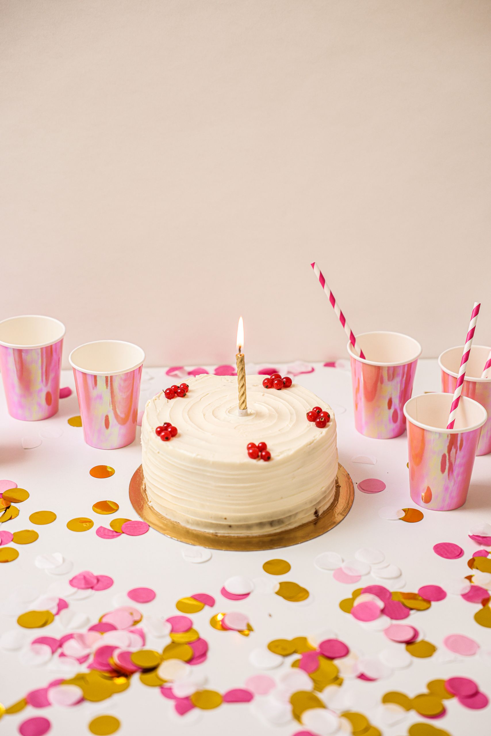 Birthday cake with a candle, surrounded by colorful cups and confetti, ready for a celebration.
