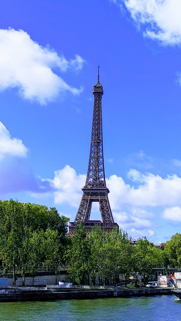 The iconic Eiffel Tower surrounded by lush greenery and a brilliant blue sky in Paris.