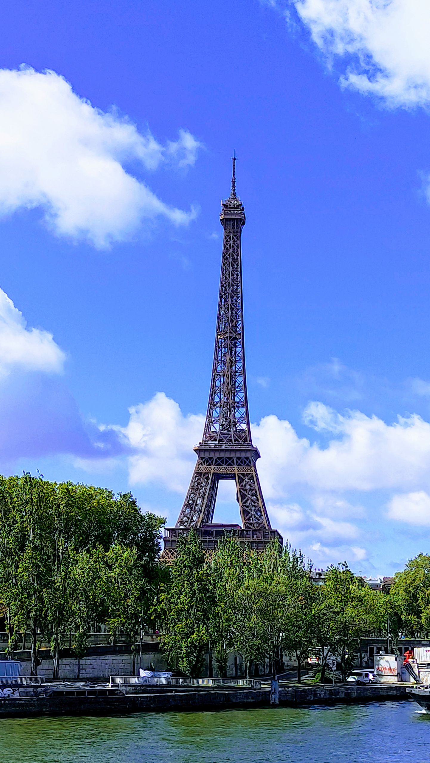 The iconic Eiffel Tower surrounded by lush greenery and a brilliant blue sky in Paris.