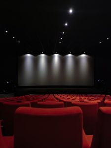 View of an empty cinema with rows of red seats and a large screen illuminated by lights.