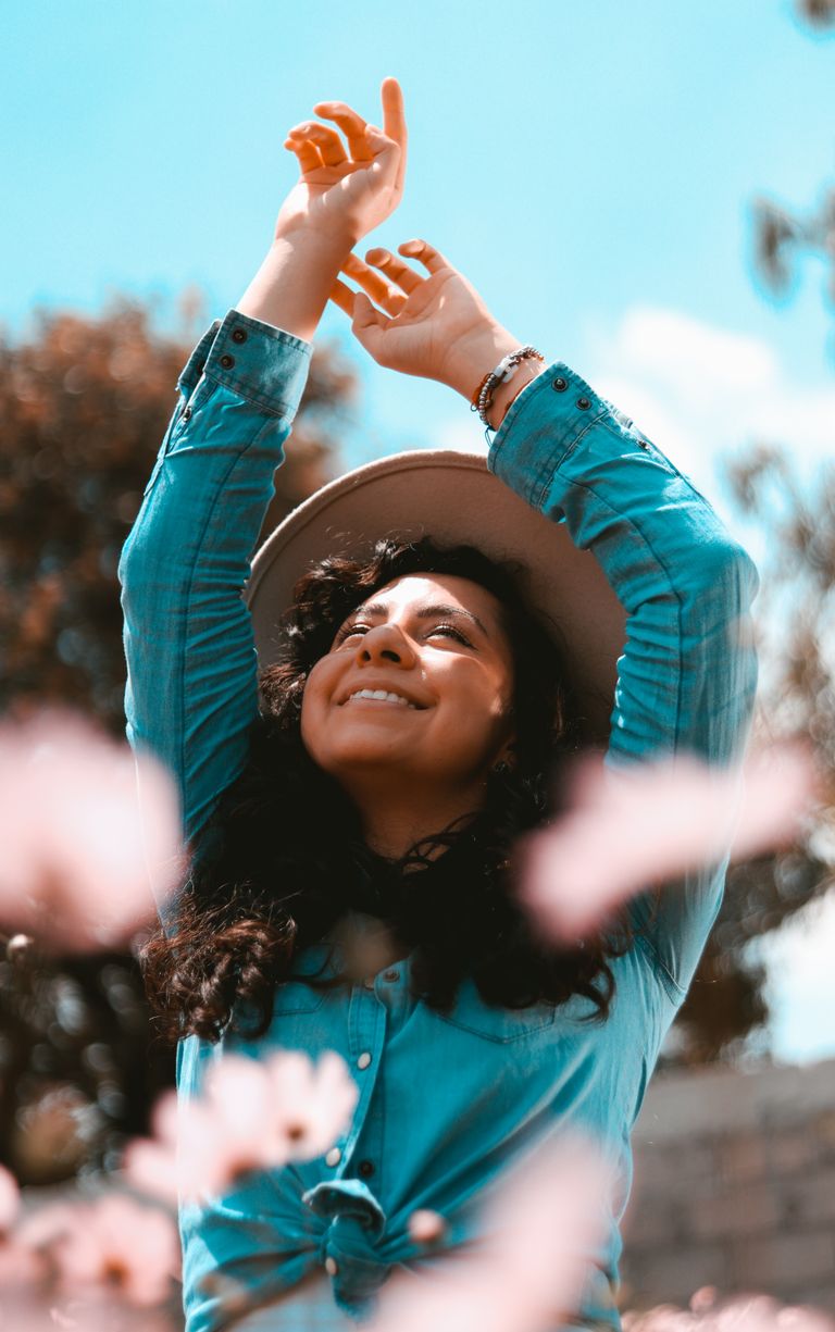 Woman with long hair and hat outdoors in spring, smiling and embracing nature.