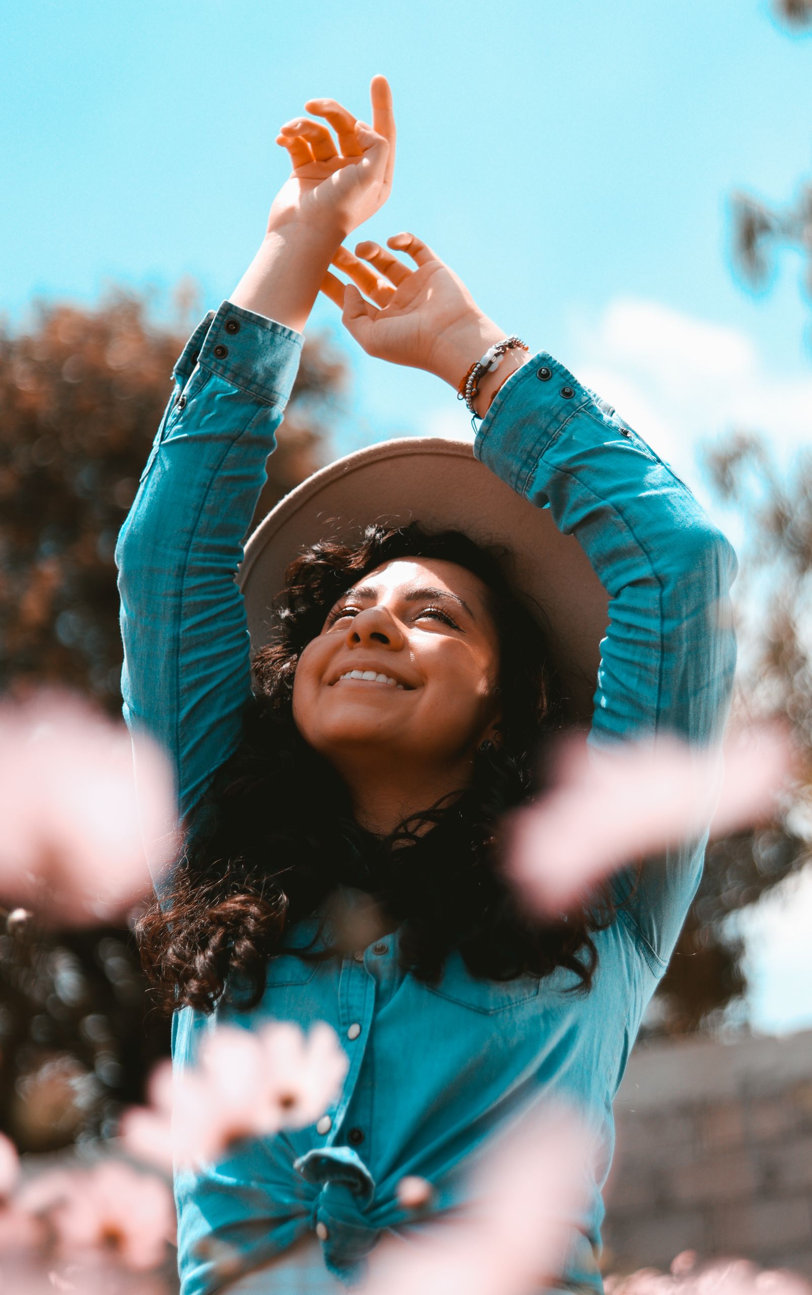 Woman with long hair and hat outdoors in spring, smiling and embracing nature.