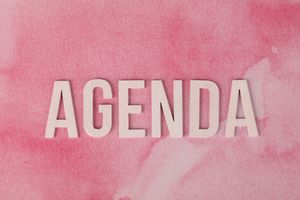 Wooden letters forming the word 'AGENDA' on a pink watercolor background.