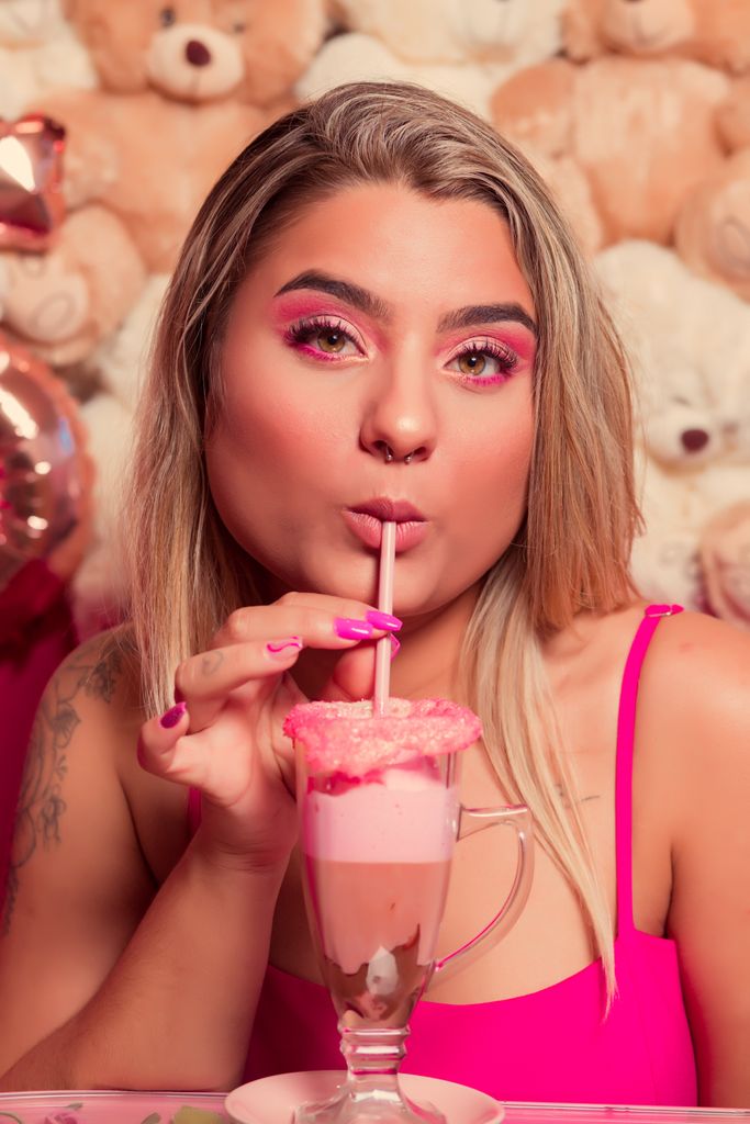 Young woman sipping a pink milkshake with teddy bears in the background, exuding a fun and girly vibe.