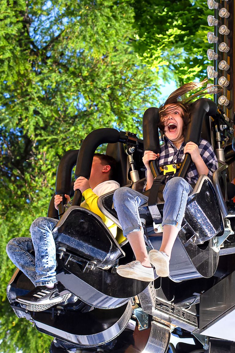 A thrilling amusement park ride with two excited young riders screaming with joy.