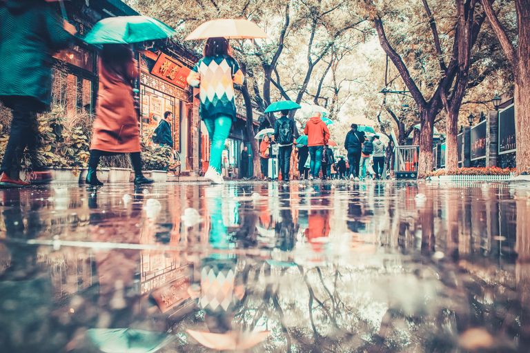 Colorful umbrellas create vibrant reflections on a rainy street in Beijing, China.