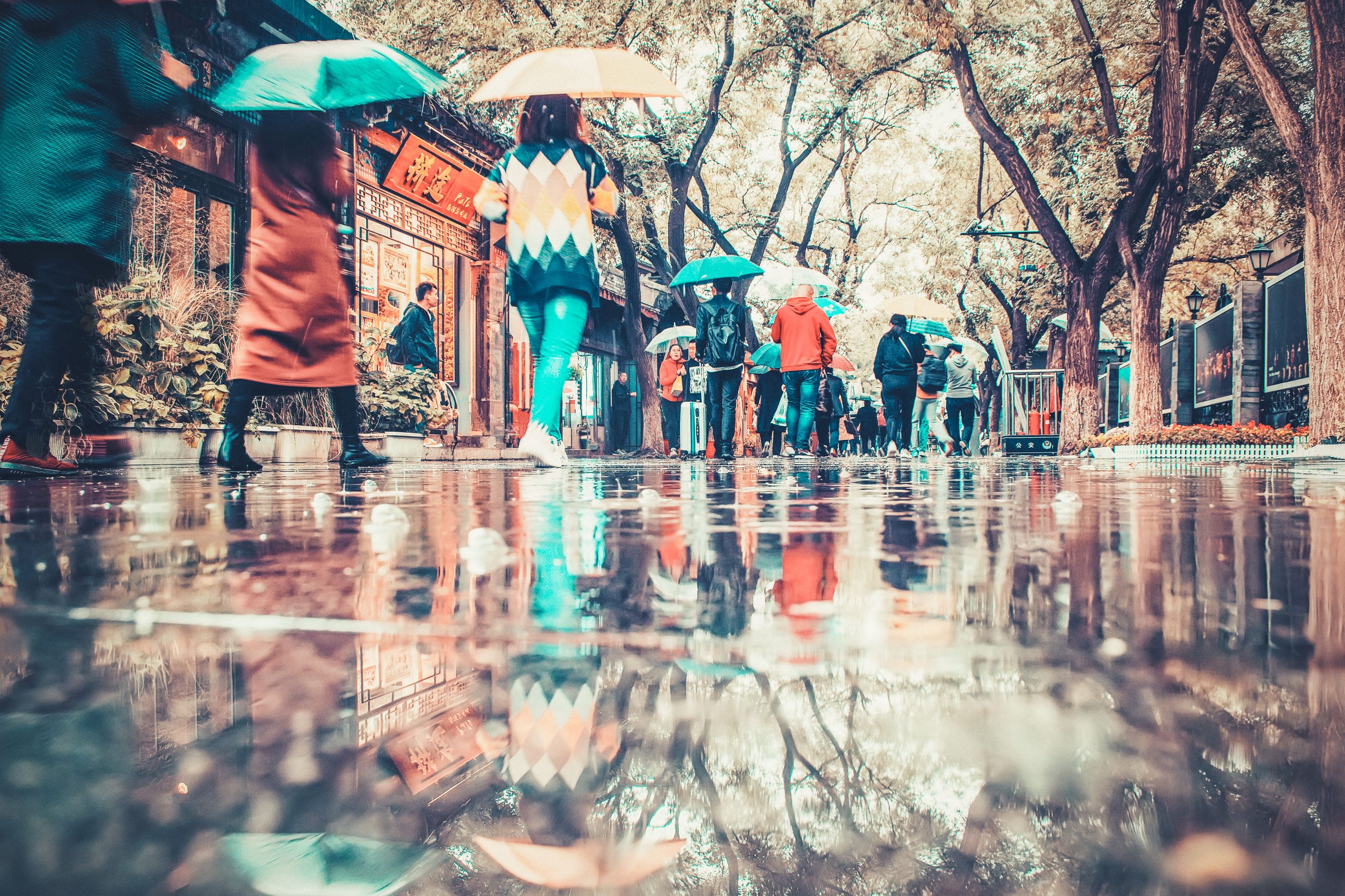 Colorful umbrellas create vibrant reflections on a rainy street in Beijing, China.