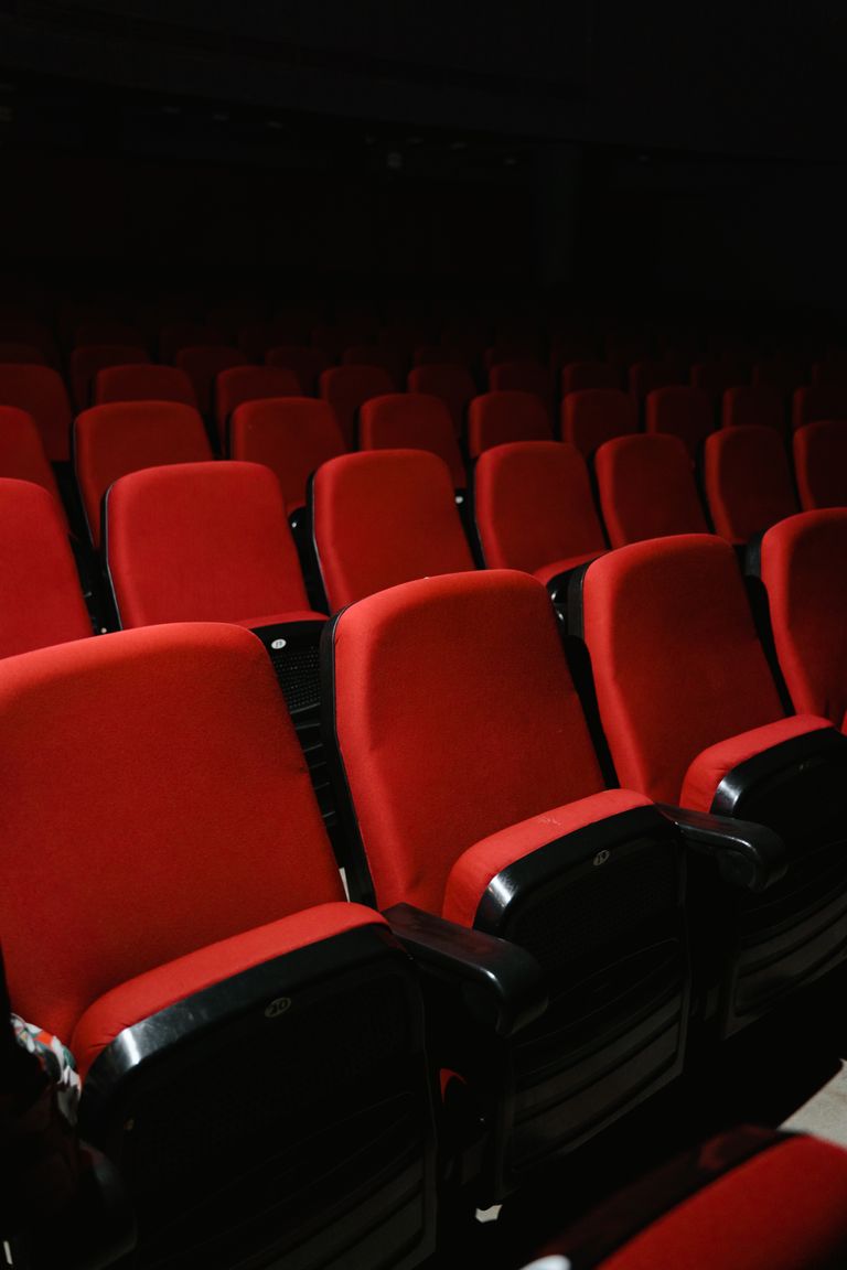 Rows of empty red theater seats in a dark cinema auditorium, awaiting audience.